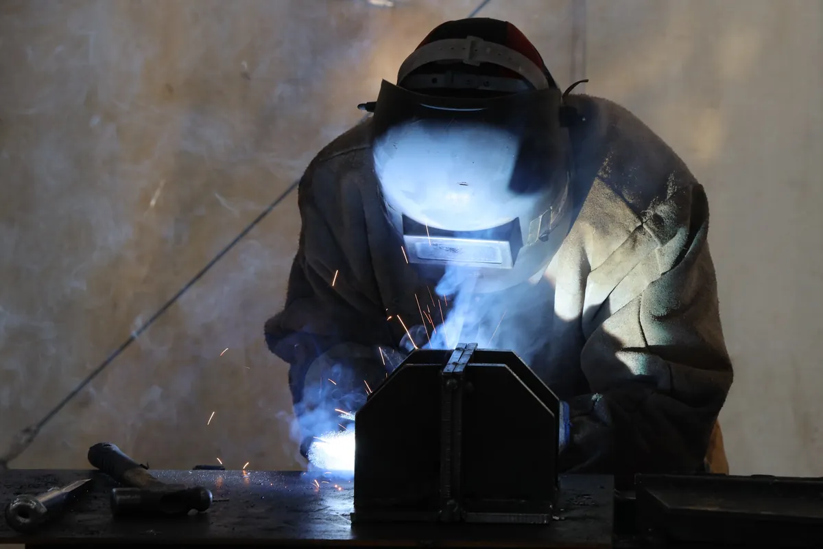 Soldador de máscara trabalhando, com o arco de solda iluminando a cena