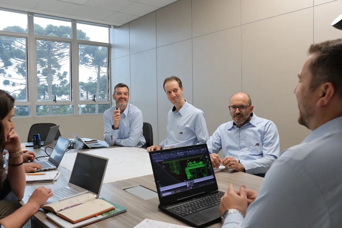 Reunião de equipe em sala clara, com notebooks e plantas sobre a mesa